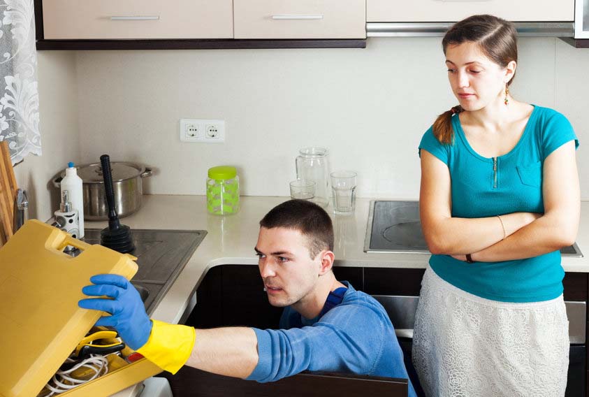 homeowner watches Plumber fixing a leak under the sink