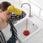 woman near clogged sink with plunger