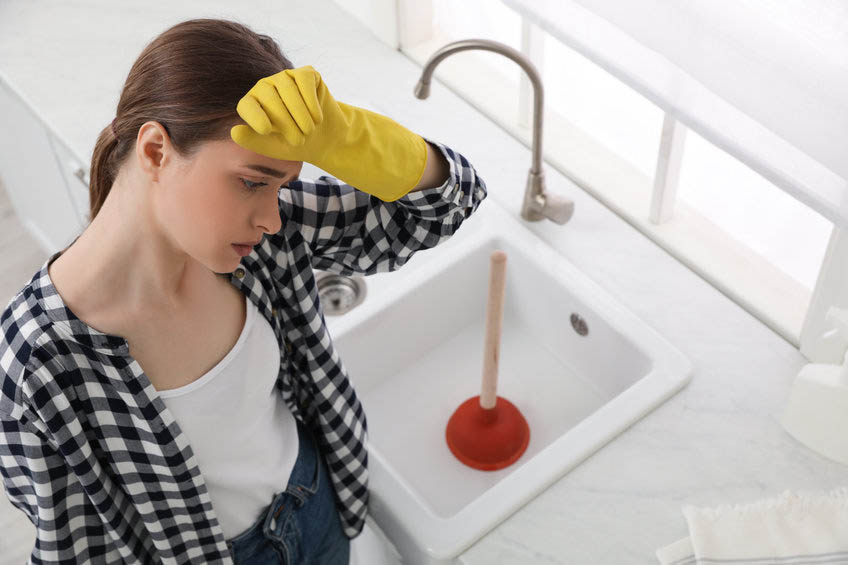 woman near clogged sink with plunger