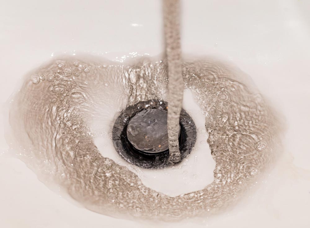 Dirty running water falling into a sink from tap